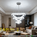3-tier silver crystal triangle LED chandelier suspended above a modern dining table, emitting warm white light – Mega Lighting